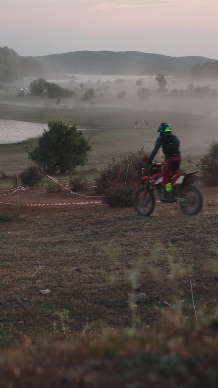 Piloto de Motocross Correndo em Pista Empoeirada Perto de Lago ao Pôr do Sol