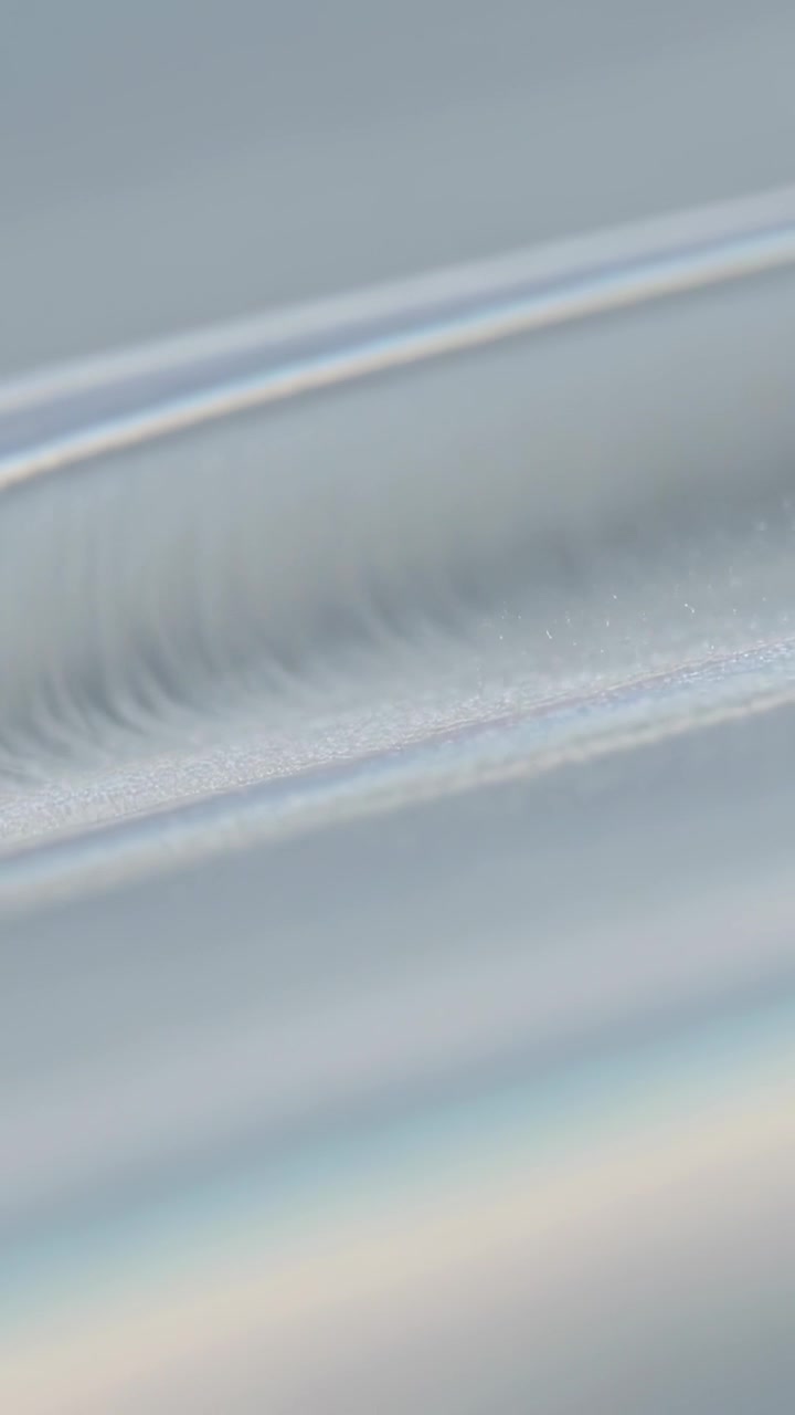 Vertical video: Shifting camera revealing curved film ridge in macro to show streaks and tiny dots