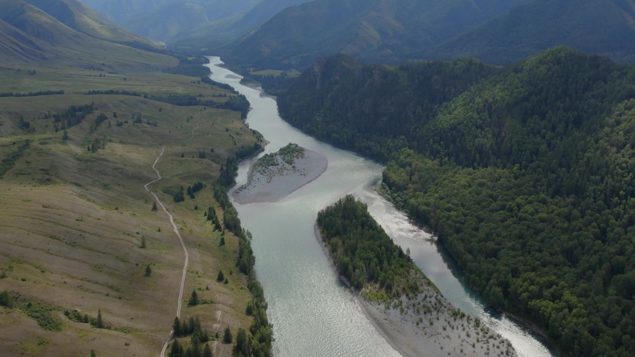 Riprese drone di un fiume tortuoso con banchi di sabbia che scorre attraverso la Valle Ak-Kem, monti Altai, Russia, con pendii boscosi e prati aperti in estate