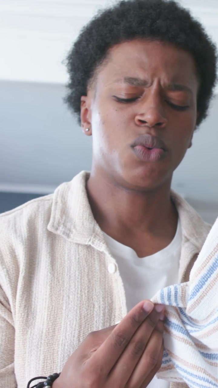 Vertical video: Picking up striped cloth, man in beige shirt inspecting fabric for stain at home
