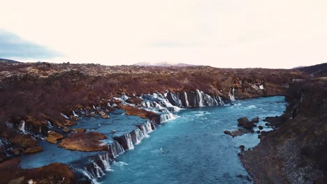 Drohne-Mit-Filmischen-Bewegungen-Zeigt-Den-Wunderschönen-Isländischen-Wasserfall-Hraunfossar-Im-Sonnenuntergangslicht-Aus-Mehreren-Winkeln