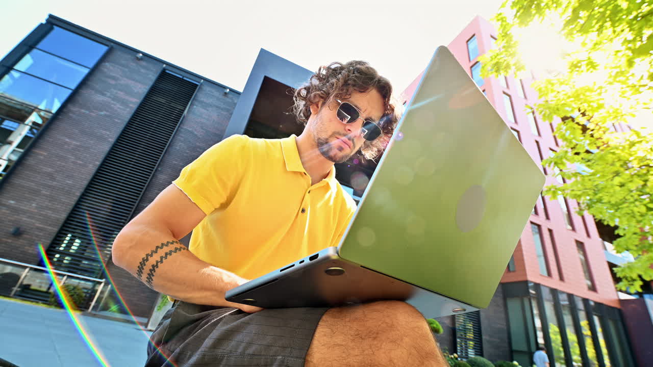 Man in yellow shirt talking standing on a bench and working on a laptop