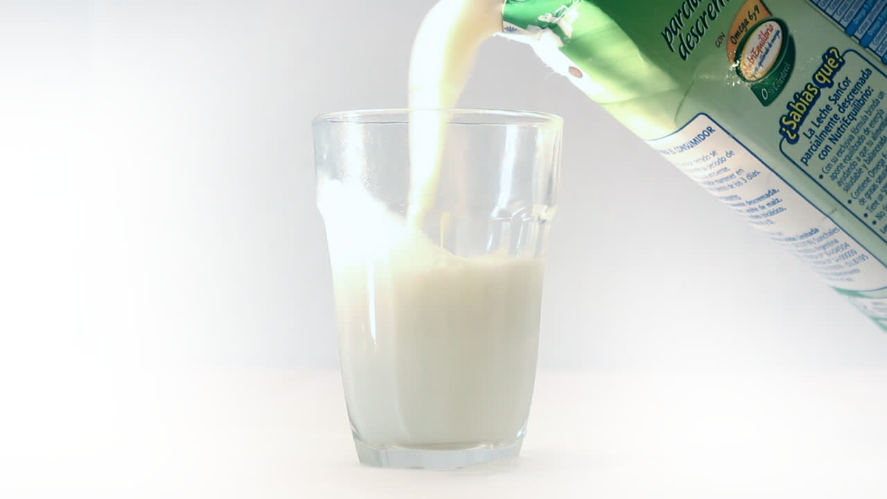Leite sendo derramado em um copo em um fundo branco