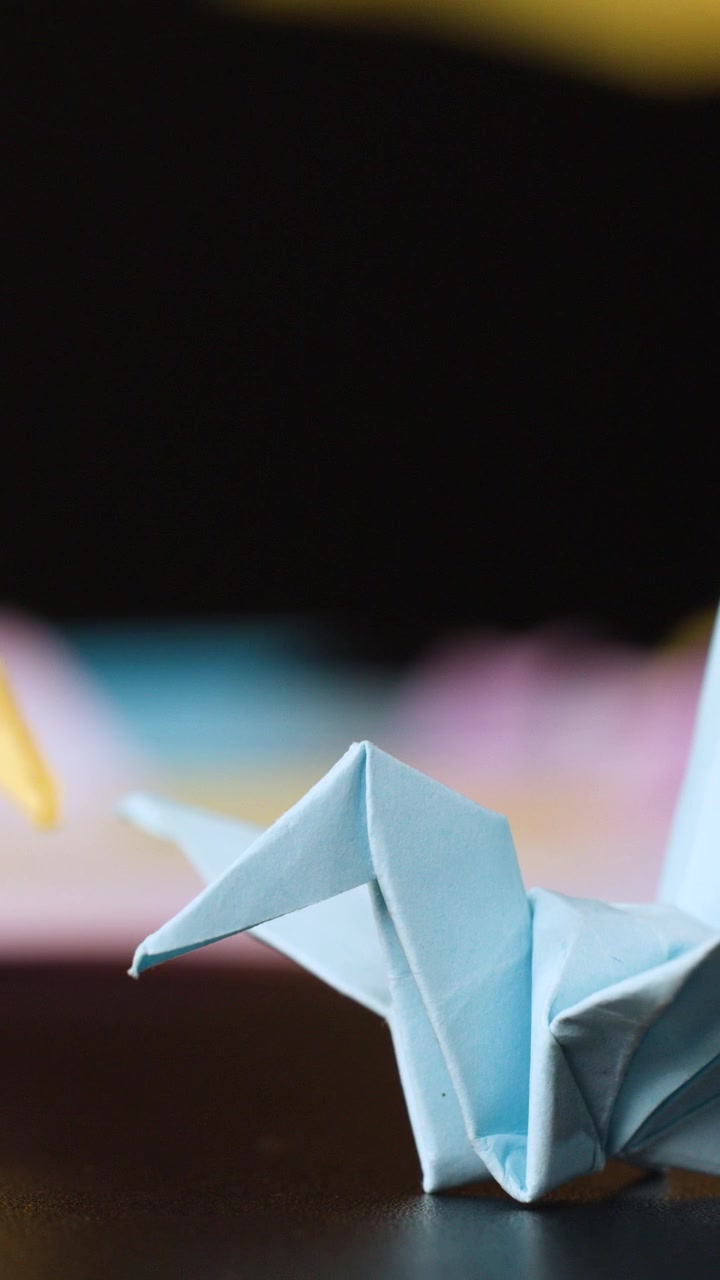 A macro shot captures folded paper cranes on a dark table with soft background lighting