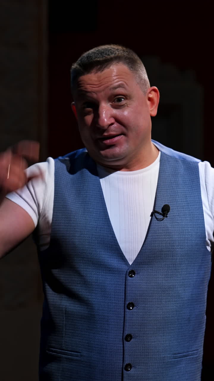 Public speaker gives performance. Middle age male entertainer, presenter or actor on stage. Man in theater wears handfree microphone. Vertical video