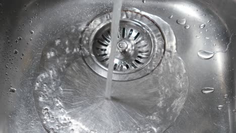 water stream from metal kitchen sink faucet draining in the sinkhole close up shot