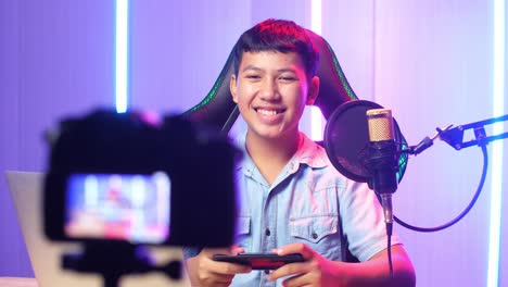 excited asian kid boy playing video game with mobile phone then smiles to camera while live stream