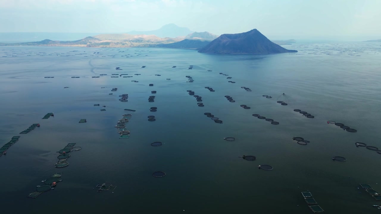 Berinayan Talisay Laurel Batangas'ta balık çiftlikleri ve volkanik manzaranın sinematik atmosferle kuşbakışı drone çekimi.