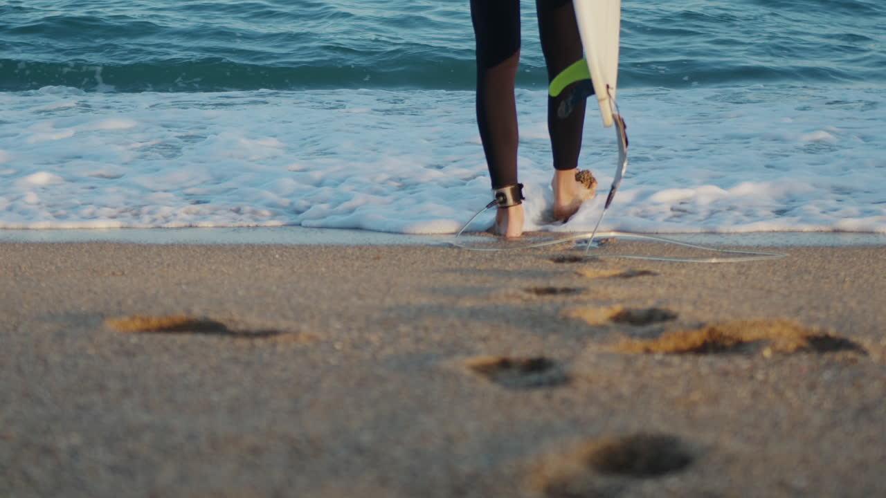 Un surfista che cammina verso la spiaggia al tramonto per prepararsi all'allenamento di surf e cercare le onde a Barcellona, Spagna, acqua, esercizio fisico in mare con la tavola, vacanza o viaggio di un uomo atletico.