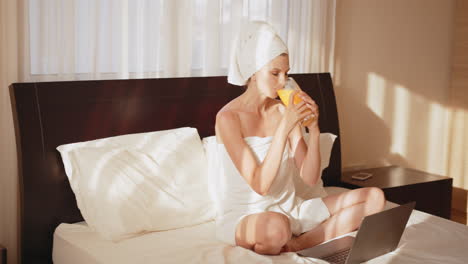 woman relaxing in bed with laptop and orange juice