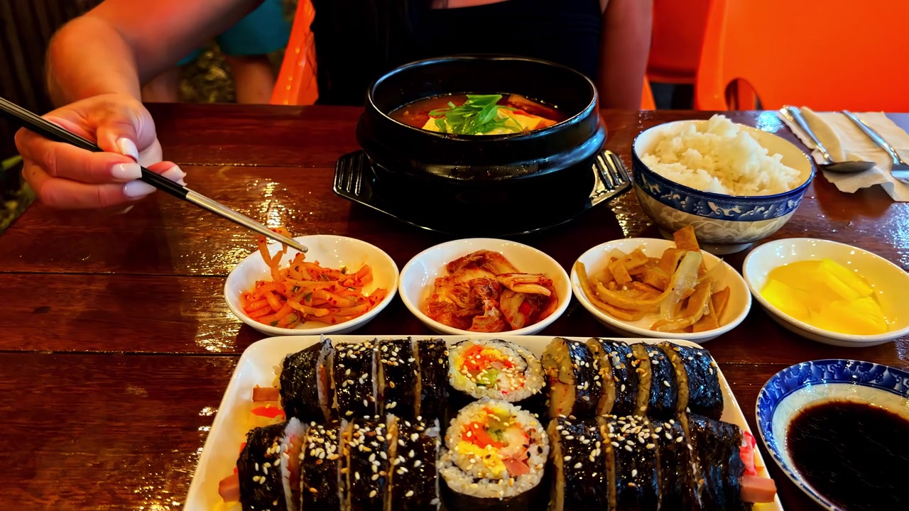 Culinária coreana com acompanhamentos variados e rolos servidos em uma mesa de madeira