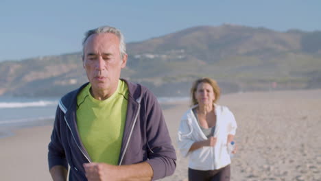 Hombre-Y-Mujer-Enfocados-Corriendo-A-Lo-Largo-De-La-Costa-Del-Océano-En-El-Día-De-Verano