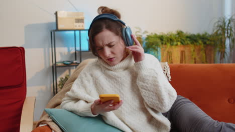 happy young woman in wireless headphones relaxing lying on sofa at home listening favorite music