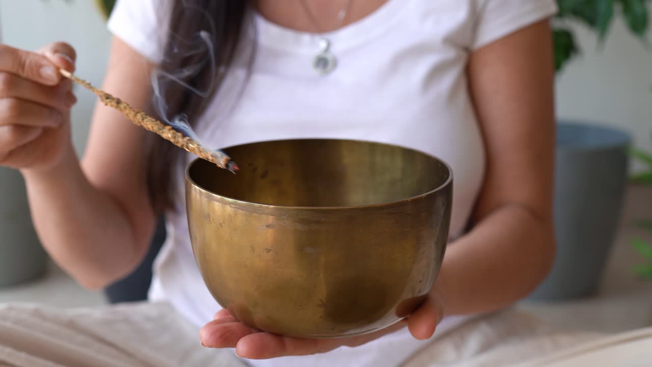 Woman Holding Brass Tibetan Bowl While Cleansing It With Lit Incense Stick. closeup shot