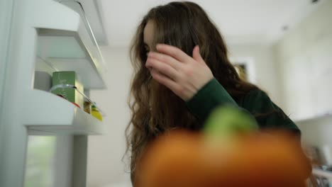 young pretty woman taking red pepper from fridge