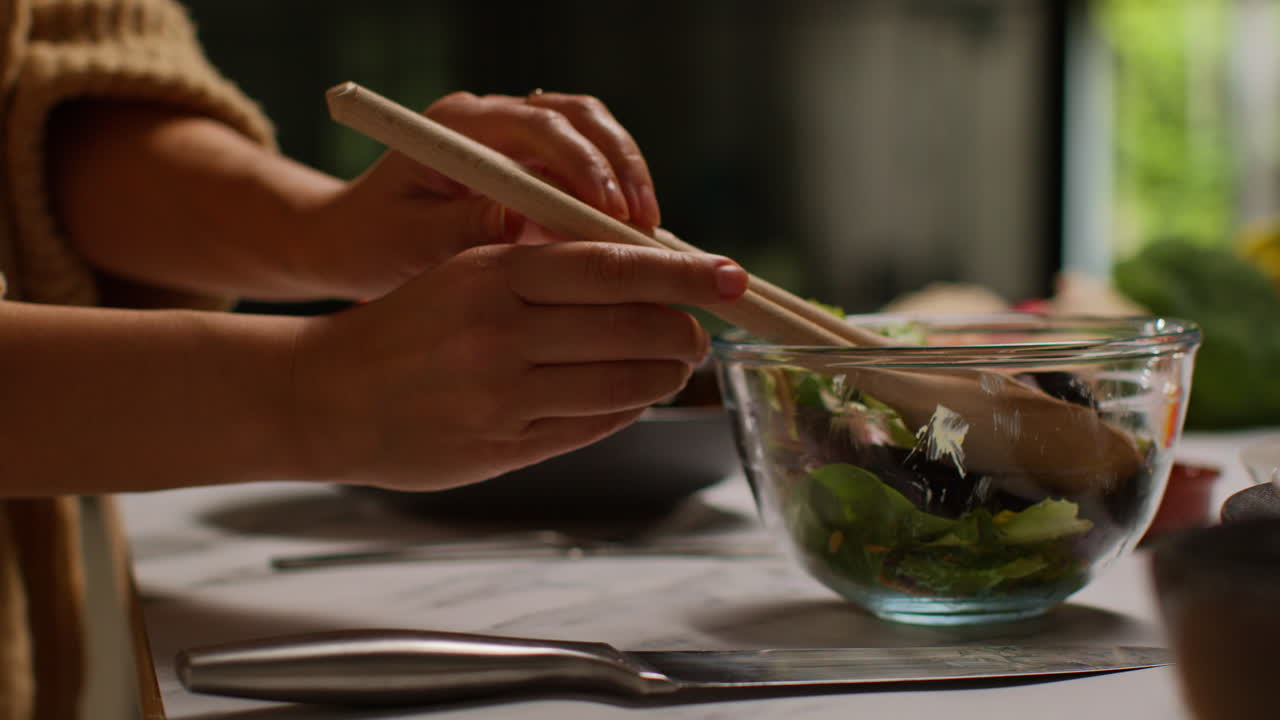 Close Up Of Woman At Home In Kitchen Preparing Healthy Vegetarian Or Vegan Meal Mixing In Spoon Of Seeds Into Bowl Of Salad Leaves