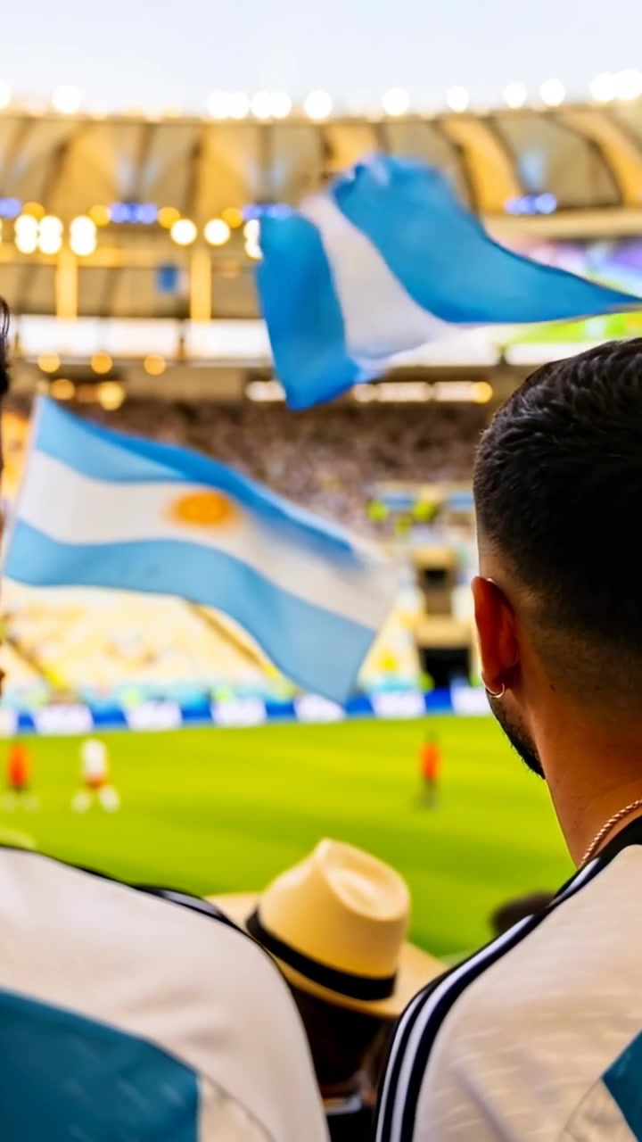 縦型動画：スタジアムでアルゼンチン代表のジャージを着てピッチでのプレーに反応し拍手するファン、旗が振られている