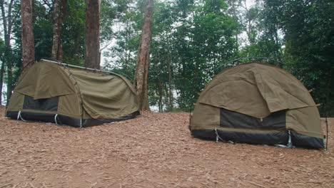 pan right, green swag tents in a camp ground next to a river surrounded by trees