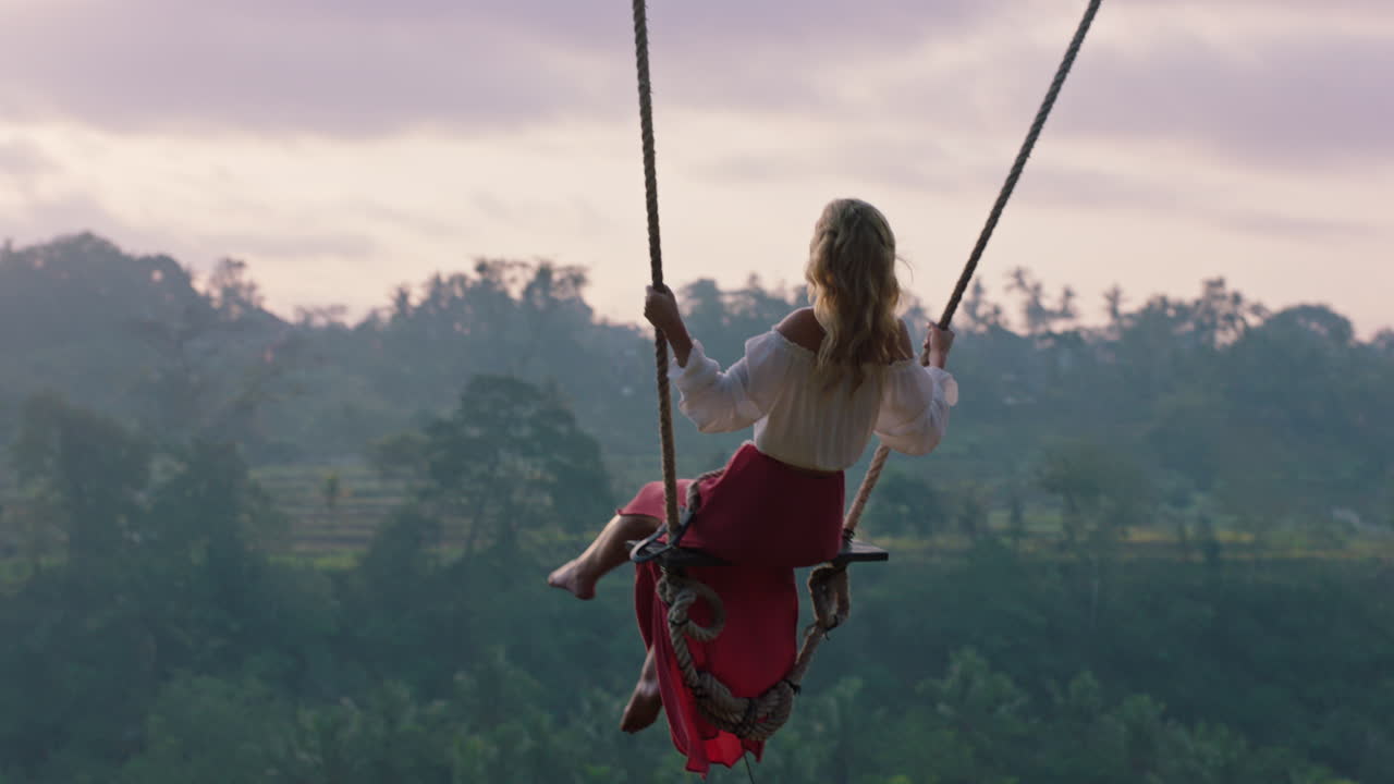 donna felice che si dondola sopra la foresta pluviale tropicale all'alba seduta su un altalena con vista panoramica godendo della libertà in vacanza divertendosi stile di vita di vacanza slow motion