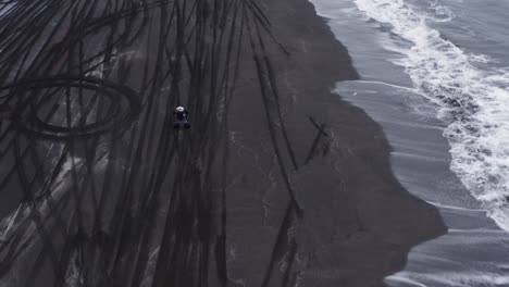 man on quad bike accelerating and pulling wheelie on black beach in iceland