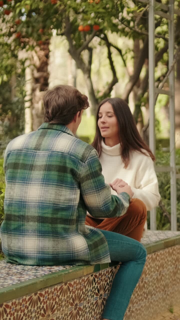 Happy young partners man and woman talking sitting in park