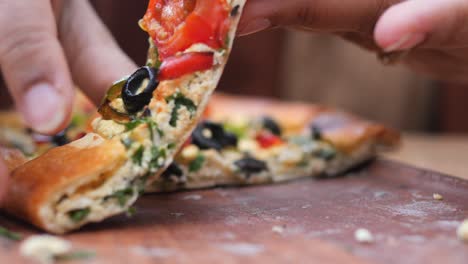 close-up of someone holding a slice of pizza with tomatoes, olives, and green peppers