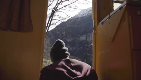 back view of caucasian man sitting on his van, pure mountains in background