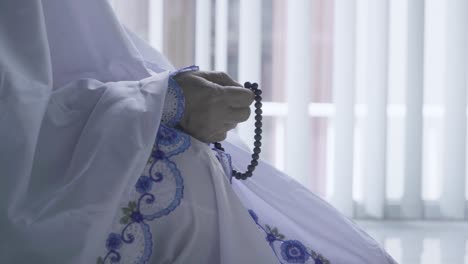 old woman hands holding beads during praying