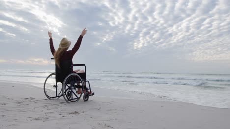 Rear-view-of-young-disabled-caucasian-woman-in-hat-sitting-on-wheelchair-and-arms-outstretched-4k