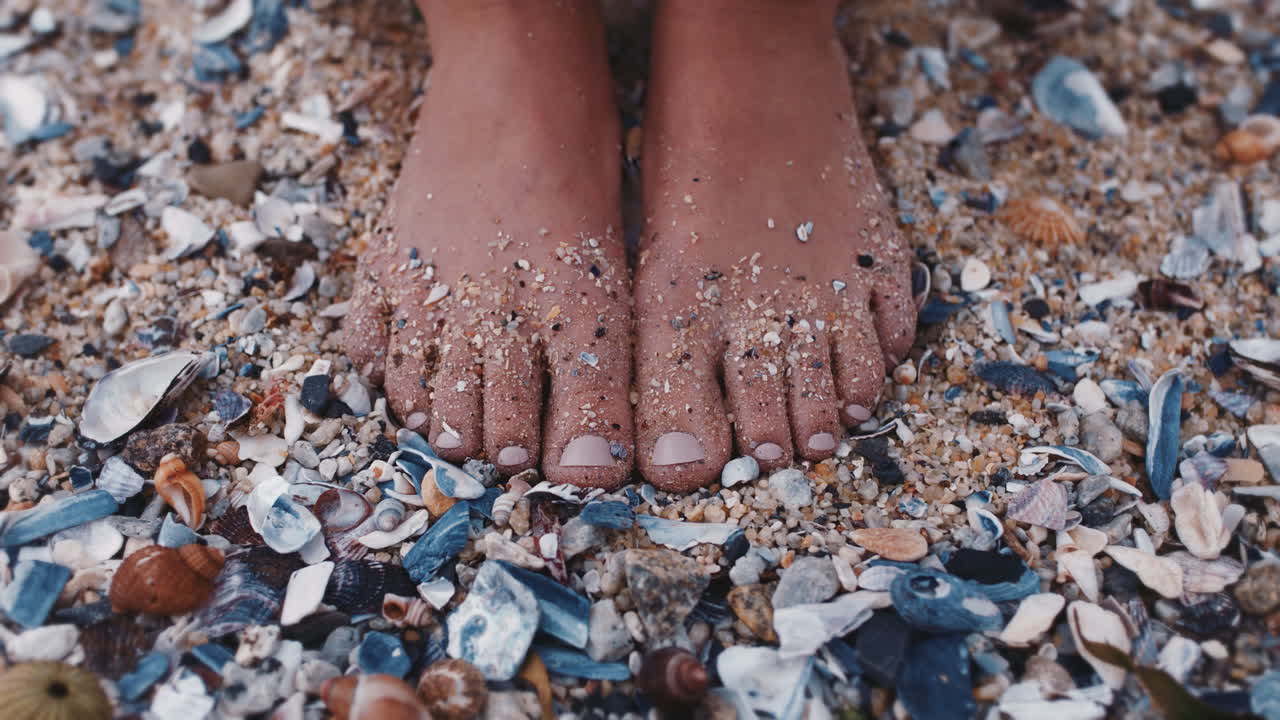 vicino piedi di donna che si muovono le dita dei piedi coperte di sabbia marina a piedi nudi godendo di bellissime conchiglie sulla spiaggia vacanza