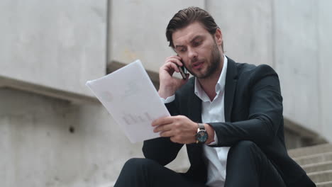 Businessman-talking-on-smartphone-with-client.Man-working-with-documents-outside