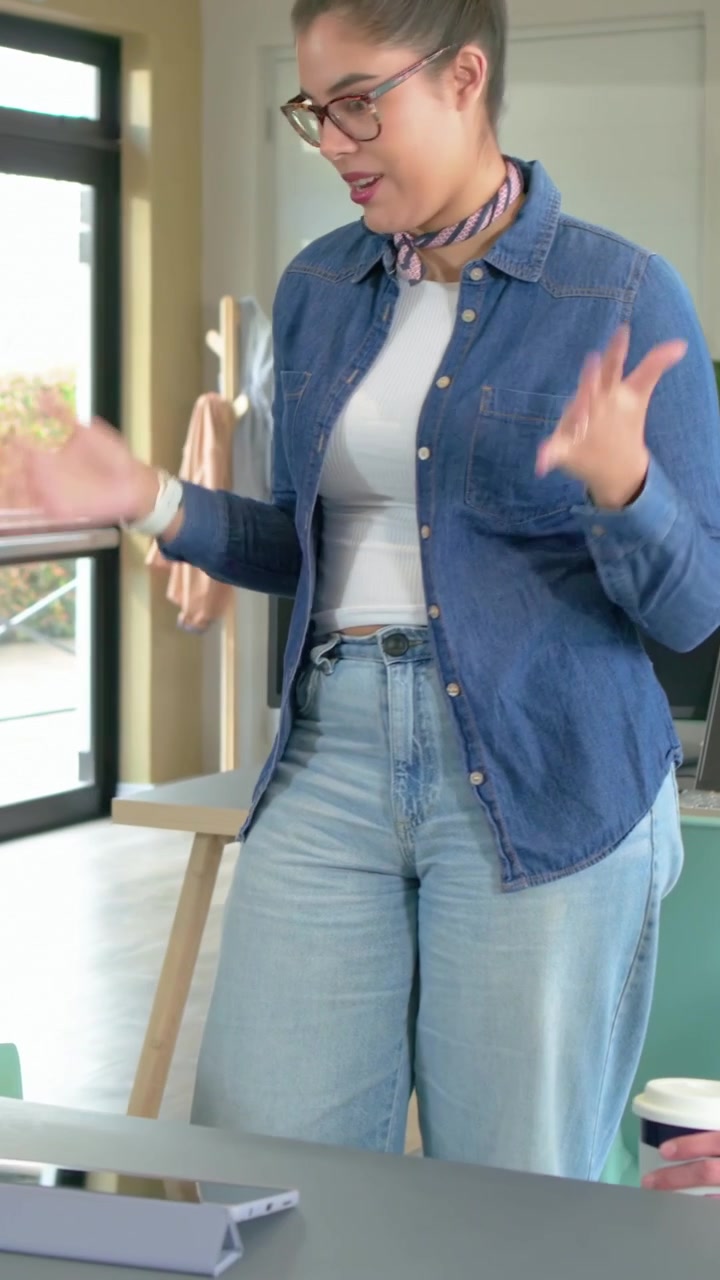 Video verticale: Donna in jeans che presenta un piano su tablet in ufficio mentre un collega indica, tenendo una tazza