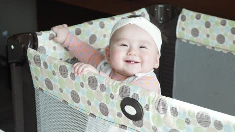 Cute-Baby-Girl-Standing-In-Her-Crib-In-A-Hotel-Room---high-angle,-close-up