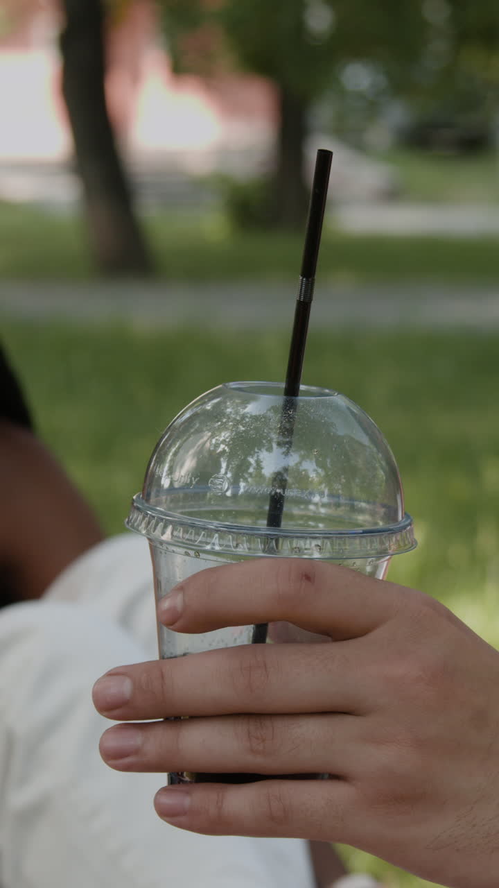 Hand holding a clear plastic cup with a straw outdoors