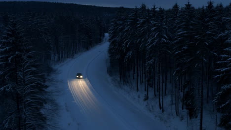 car driving on a snowy road through a forest at night