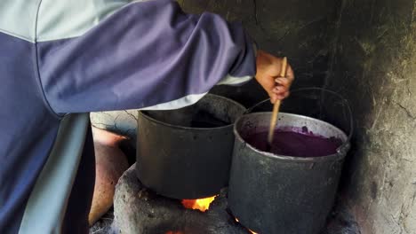 close up of quechua artisan stirring alpaca wool in a pot of purplevcolored natural dye made from local plants, boiling over an open flame near cusco, sacred valley, peru
