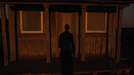 shadow of a person in front of a wooden cabin at sunset