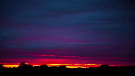 amazing colorful sunset above the forest trees with purple and red clouds flowing - time lapse