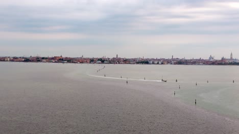 aerial flyover of a boat cruising on a bay with the venice skyline on the horizon, italy.