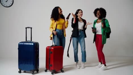 three diverse young women with suitcases, happily interacting while preparing for travel