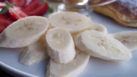 closeup of sliced banana on a plate with pancakes and strawberries