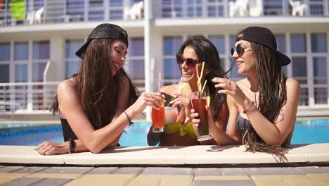 beautiful young girls in sunglasses drinking cocktails relaxing by the pool. summertime pool party. slowmotion shot