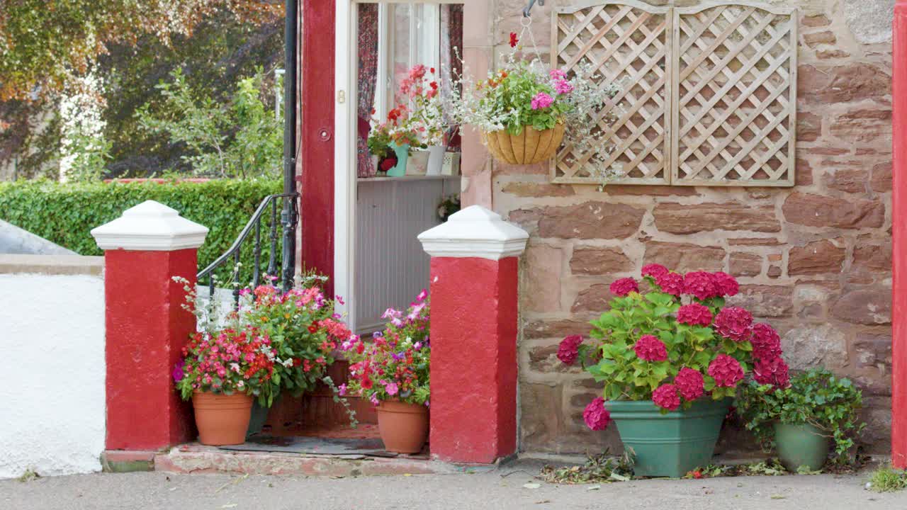 A smooth daylight pan reveals a classic red telephone box, stone wall, and vibrant potted flowers in a quaint Edinburgh garden setting