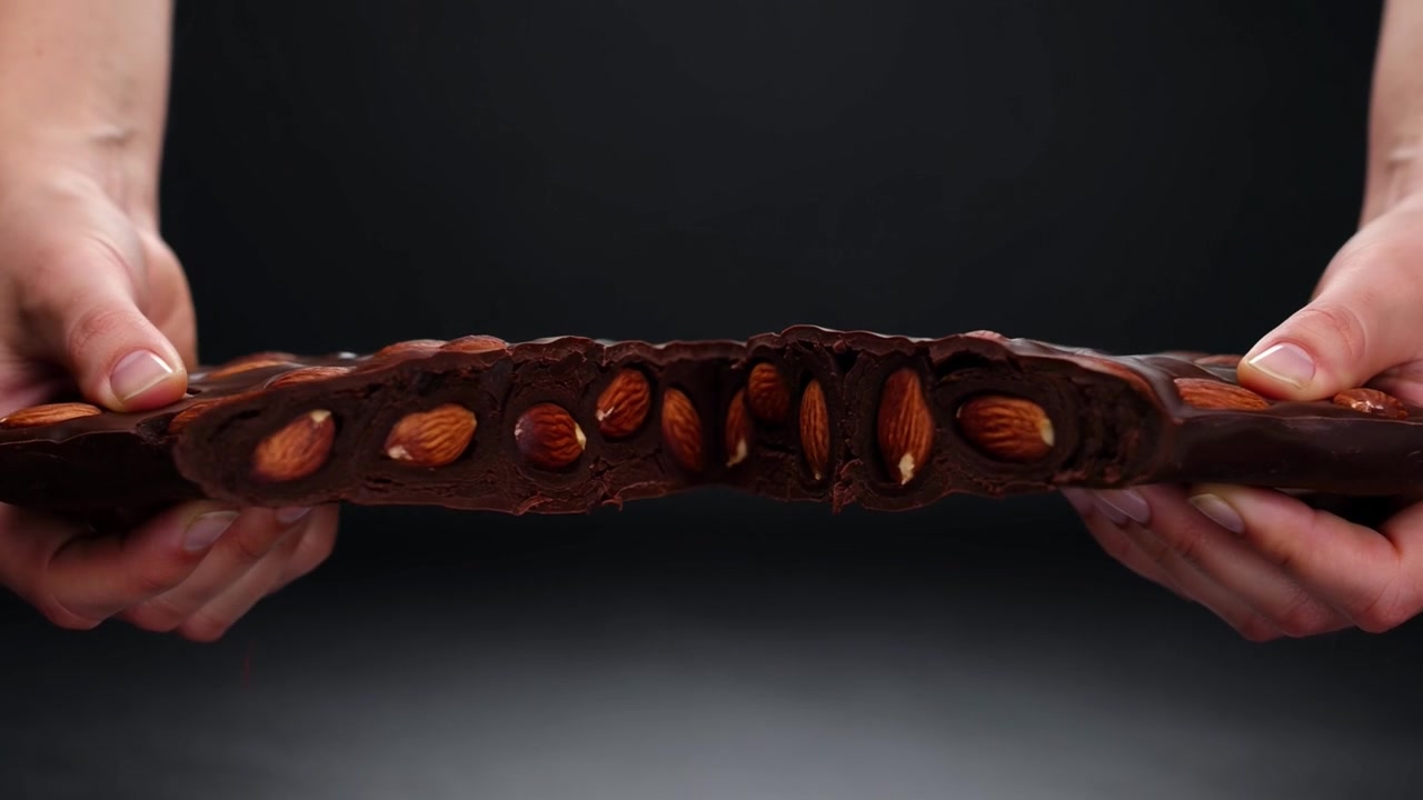 Hands Breaking a Bar of Dark Chocolate with Whole Almonds