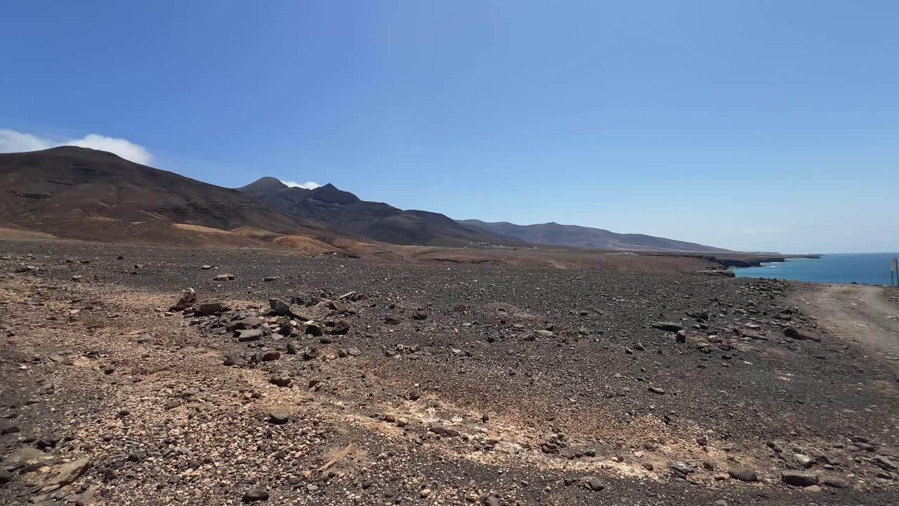 Guida in POV attraverso il paesaggio vulcanico brullo della penisola di Jandía durante il tour per la spiaggia di Cofete, Fuerteventura, con l'oceano visibile. Isole Canarie, Spagna.