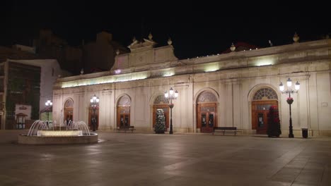 Vista-Nocturna-Del-Edificio-Del-Mercado-Central-Y-La-Fuente-En-La-Plaza-Mayor-Vacía,-Castellon-De-La-Plana,-España