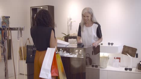 positive female cashier operating payment process and giving shopping bag to the customer