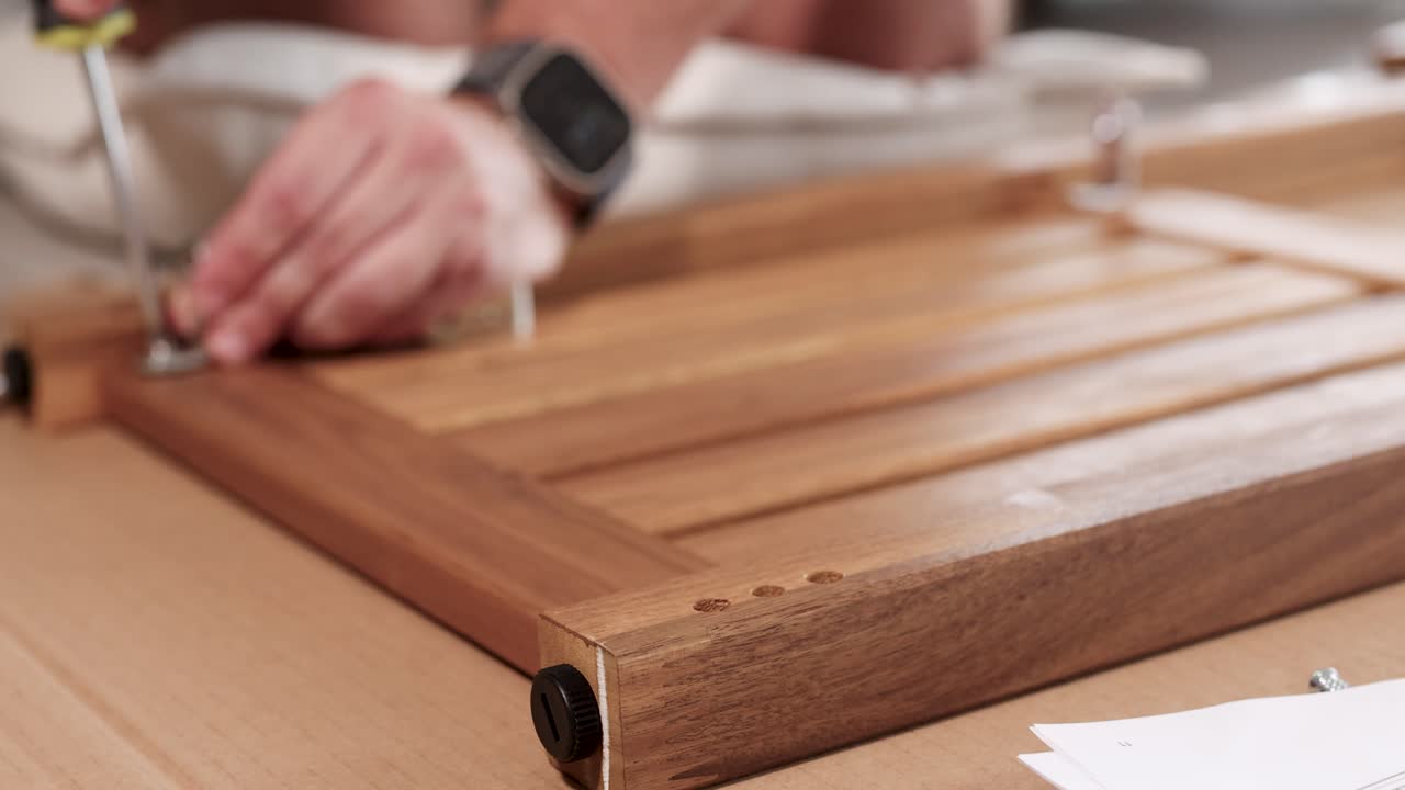 Hands assembling wooden furniture using a screwdriver in a well-lit workshop. Close-up shots highlight precision and craftsmanship