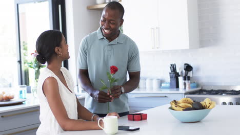 Una-Pareja-Afroamericana-Comparte-Un-Momento-Alegre-En-La-Cocina,-Intercambiando-Regalos.