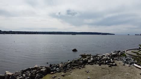 Aerial-fly-over-seawall-park-by-the-ocean-where-boats-are-in-the-rocky-harbor-on-a-low-tide-scenic-spring-afternoon-as-the-waters-are-calm-and-partly-cloudy